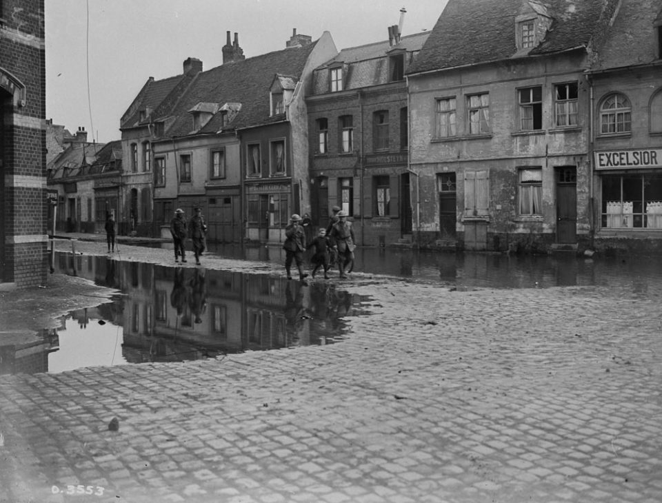 Canadians escorting a French girl through the flooded streets of Valenciennes (LAC M#3397417).